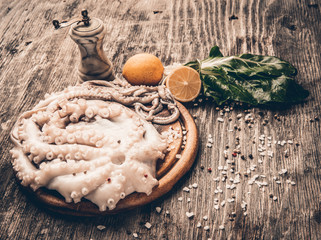 Whole fresh raw octopus on cutting board with lemon and pepper