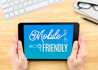 Hand holding tablet with Mobile friendly word on wood table ,Dig