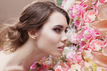Fototapeta premium Portrait of beautiful fashion girl, smelling a many flowers. Beautiful makeup and messy romantic hairstyle. Flowers background. Green eyes. 