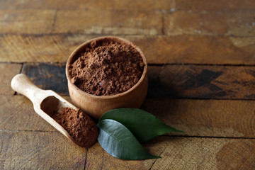 Bowl with aromatic cocoa powder and green leaf on wooden background, close up