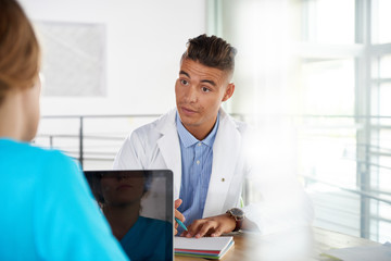 Fototapeta premium Team of doctor and nurse discussing a patient diagnosis sitting at the desk in bright modern office