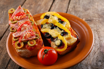 Hot pizza baguettes with olives, paprika, tomatoes and ham on wooden table