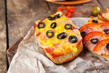 Hot pizza baguettes with olives, paprika, ham and salami on wooden table