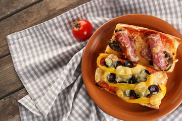 Hot pizza baguettes with paprika, bacon, olives and cheese on wooden table