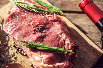 Raw pork steak with bottle of red wine and rosemary wooden background