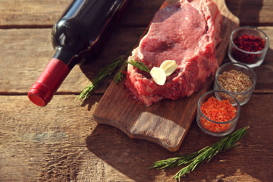 Raw pork steak with bottle of red wine and spices on wooden background