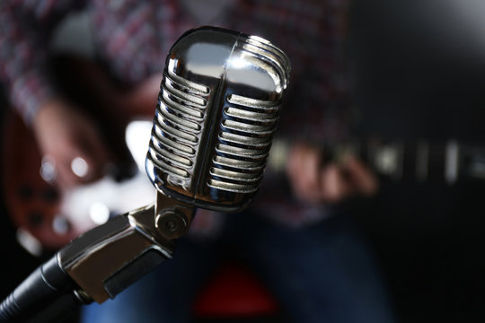 Microphone and young man playing electric guitar on dark background