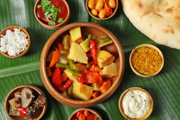 Stewed vegetables with spices and flat bread on banana leaf background