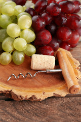 Wine cork and tailspin with bunch of grapes on wooden background