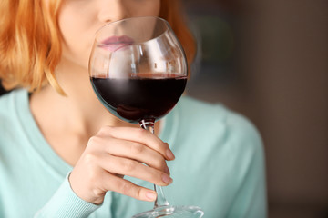 Young woman with glass of red wine on light blurred background