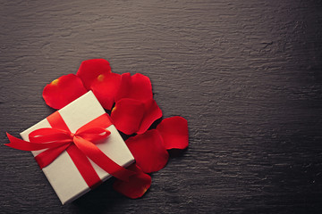 Gift box, rose petals and decorative hearts on wooden background