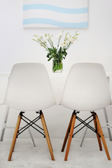 Modern dining room. White chairs and table with bouquet of flowers, abstract picture on the wall