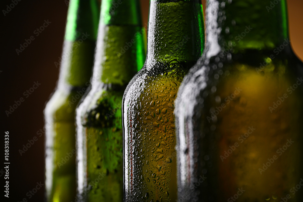 Wall mural Four green glass bottles of beer on dark lighted background, close up