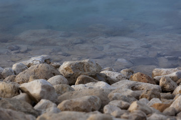 White yellow grey natural boulders with salt levee on blue water edge of Dead Sea
