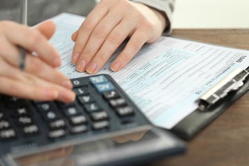 Fototapeta na wymiar Female hand holding a pen and using calculator while filling in the individual income tax return, close up