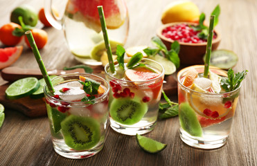Refreshing cocktails with ice, mint, pomegranate seeds and slices of fruits on wooden background