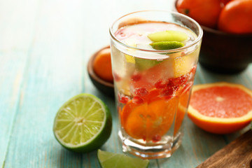 Refreshing cocktail with ice, mint, pomegranate seeds and slices of fruits on blue wooden background
