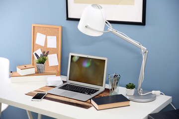 Workplace with laptop, mobile phone and table on blue wall background
