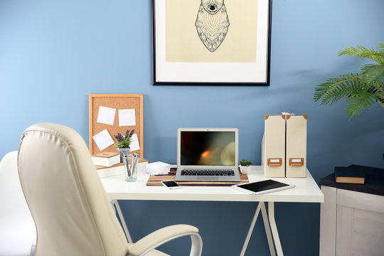 Workplace with different devices, stationery and table on blue wall background