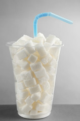 Plastic glass full of sugar with straw on grey background