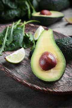 Sliced avocado with lime, spinach and arugula on wooden plate