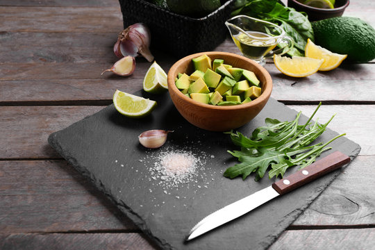 Diced avocado in wooden bowl with lime, garlic and arugula on slate plate