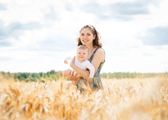 Beautiful woman playing with her infant baby in a meadow of whea