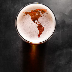 American beer concept, America silhouette on foam in beer glass on black table. The continents shapes are altered ones from visibleearth.nasa.gov