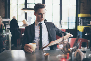 Single young man in suit reading newspaper in bar