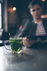 Cup of fresh mint tea with blurred man with tablet in bar