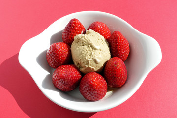 Homemade tiramisu ice cream / gelato on a white porcelain plate surrounded by whole upright standing fresh strawberries on red background
