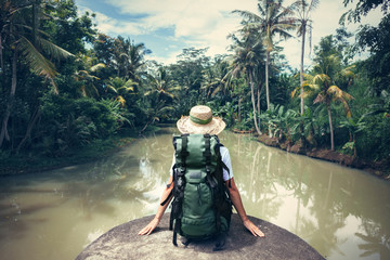 Woman traveler with backpack sitting on the edge and looking at tropical river (intentional vintage...