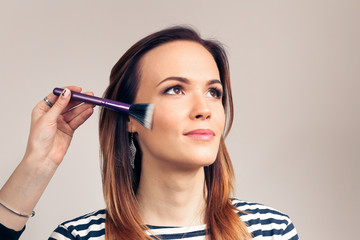 Obraz premium Makeup artist applying liquid tonal foundation on the face of the woman. Beauty Girl with Makeup Brush. Natural Make-up for Brunette. 