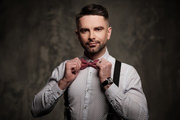 Stylish man with bow tie wearing suspenders and posing on dark background.