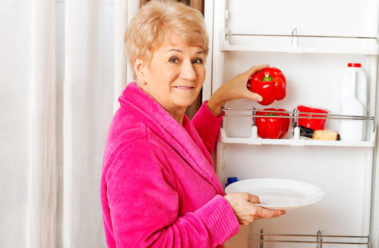 Senior woman taking a red paprika from fridge