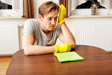 Tired man sitting behind the desk with cloth and gloves