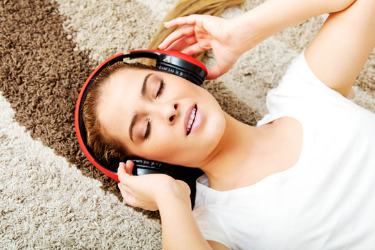 Young woman lying on the carpet and listenig a music in headphones