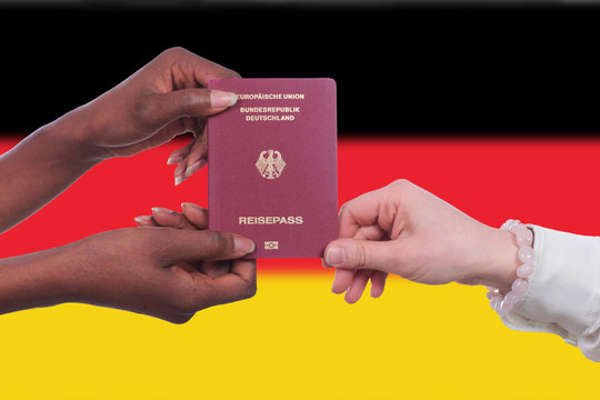 Schwarze und weiße Hand halten einen deutschen Pass vor Deutschland Fahne
