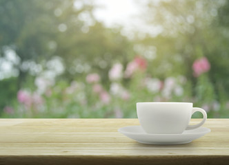 White cup on wooden table with blurred pink flower and tree, sof