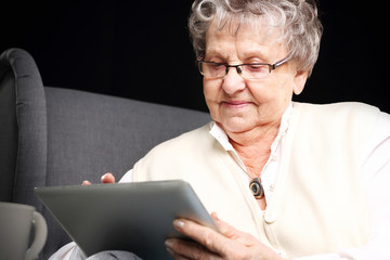 Starsza kobieta z tabletem.Starsza kobieta serfuje po internecie. - obrazy, fototapety, plakaty