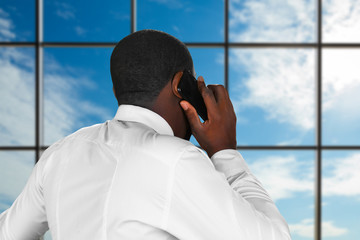 Afro man holding mobile phone. Chief's phonecall on sky background. Crucial moment for company's executive. Waiting for important news.