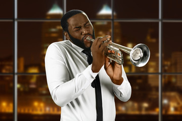 Man in shirt playing trumpet. Black trumpeter in night city. Concert for jazz lovers. Live performance of awesome music.