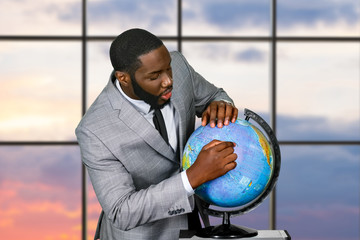 Black businessman pointing at globe. Man studying globe at sunrise. The global plan. Somewhere...
