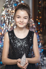 Young beautiful girl smiling and holding a Christmas tree. In black dress happy.