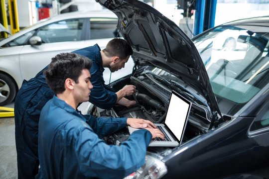 Mechanics examining car engine using laptop