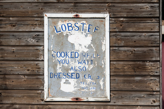 Lobster, seafood: Old wooden sign on an exterior wall with rotten capitals