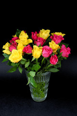 Bouquets of fading yellow and pink roses in a glass vase