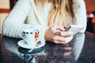Close up on the hand of a young woman sitting on a bar having a coffee, smart phone hand hold, tapping the screen - leisure, technology, social network concept