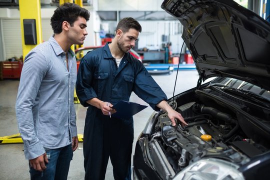 Mechanic showing problem with car to customer in garage