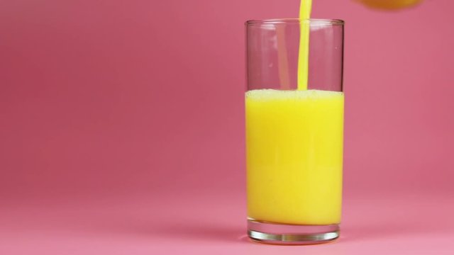 Orange juice in glass and bottle on pink background